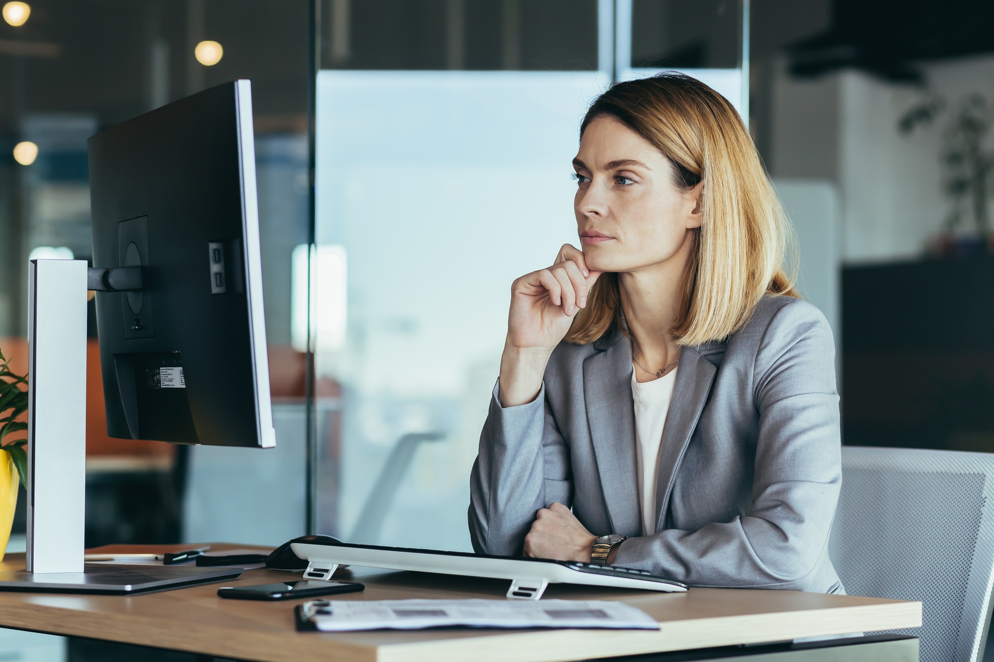 Thinking business woman looking at computer monitor, business woman working in modern office